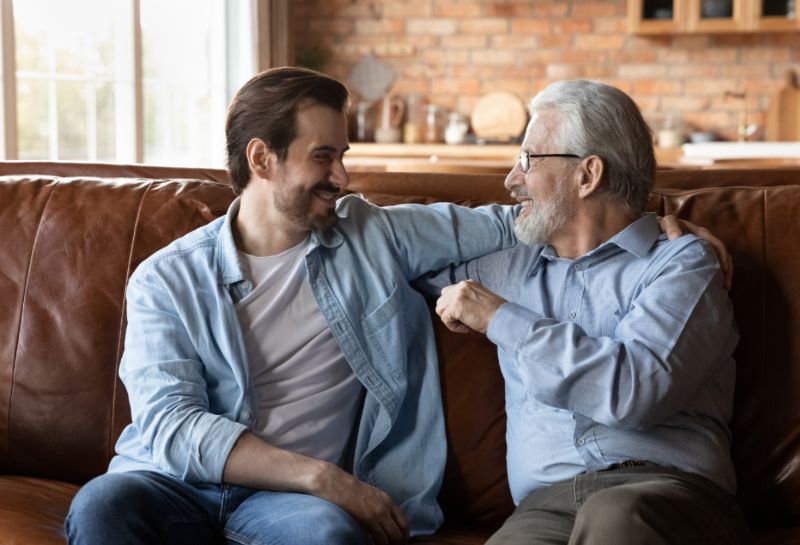 Adult man and older adult sitting and talking on couch
