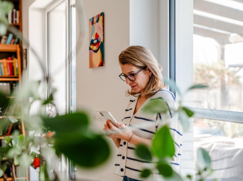 women looking at phone relaxing by window