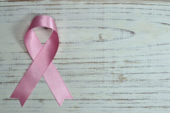Pink breast cancer awareness ribbon on a weathered white wooden surface, representing breast cancer caregiver support.