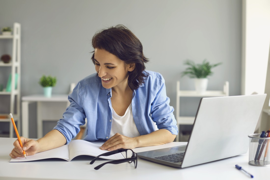 A woman does research on a laptop and takes notes in a notebook