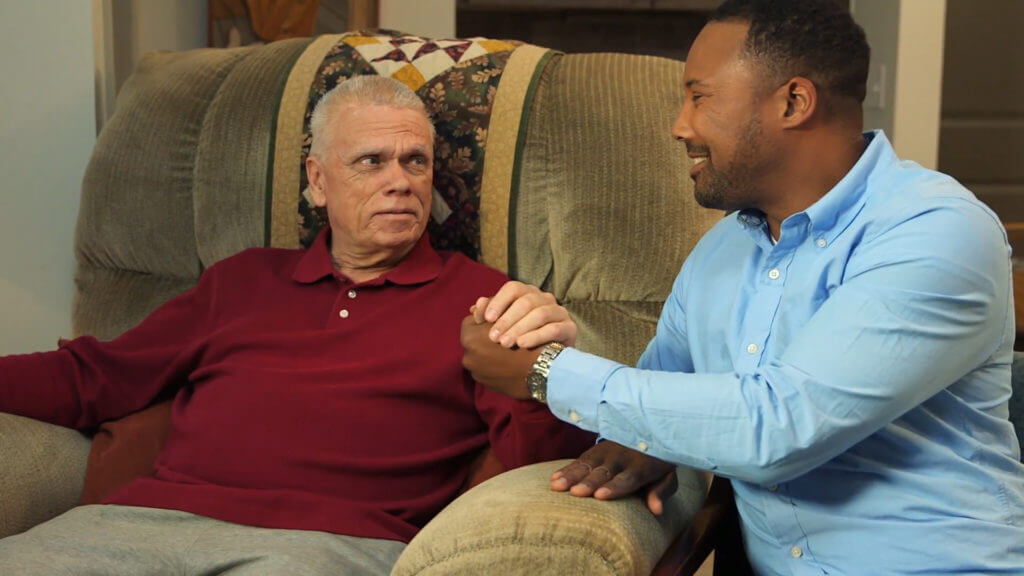 Older man holding home nurse's hand