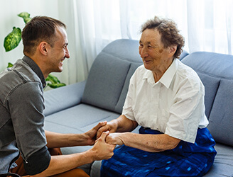 Younger home nurse holding hands of older man