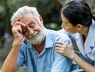 A man holds his head while supported by his nurse.