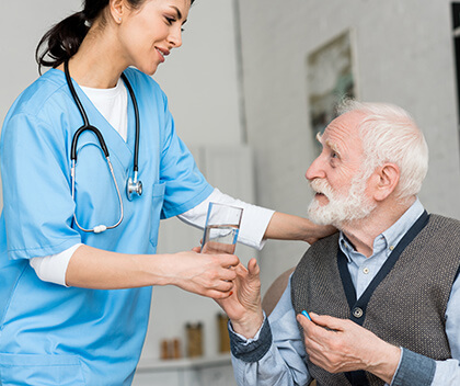 Young nurse giving water to older patient