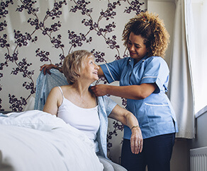 Young nurse helping older woman dress