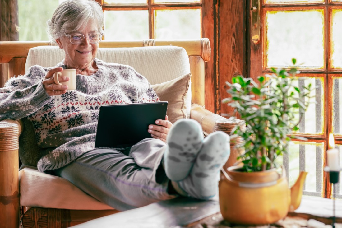 An older woman wearing a sweater drinks coffee in her cozy northern home