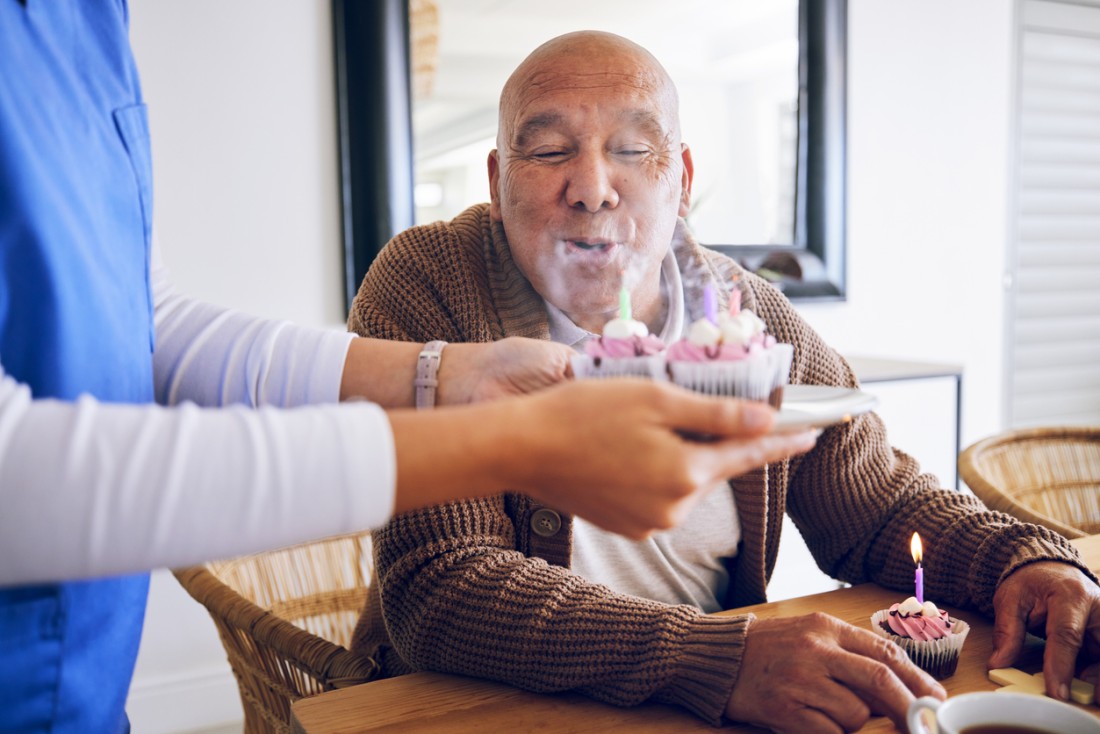 A caregiver brings a plate of birthday cupcakes to a client