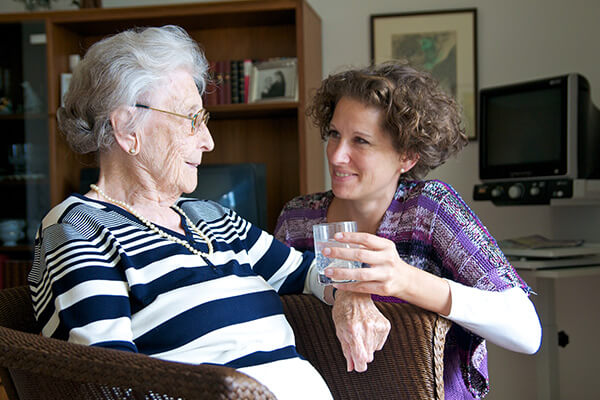 Home nurse holding glass in front of older woman