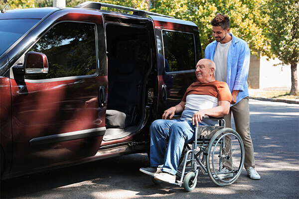 Home nurse helping older man in wheelchair into vehicle