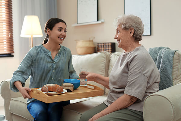 Young nurse bringing older woman food