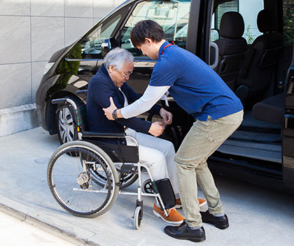 A nurse helps an old man from the car to his wheelchair.