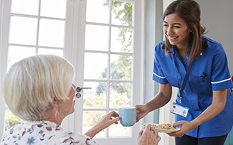 Home nurse giving an older woman a mug of tea