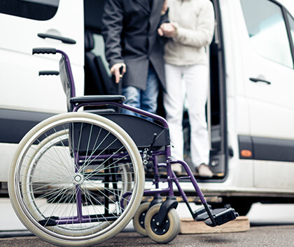 A nurse helps an old man from the car to his wheelchair.