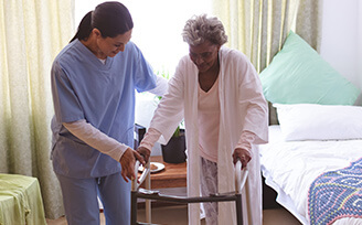 Young nurse helps elderly woman get out of bed and walk to her walker