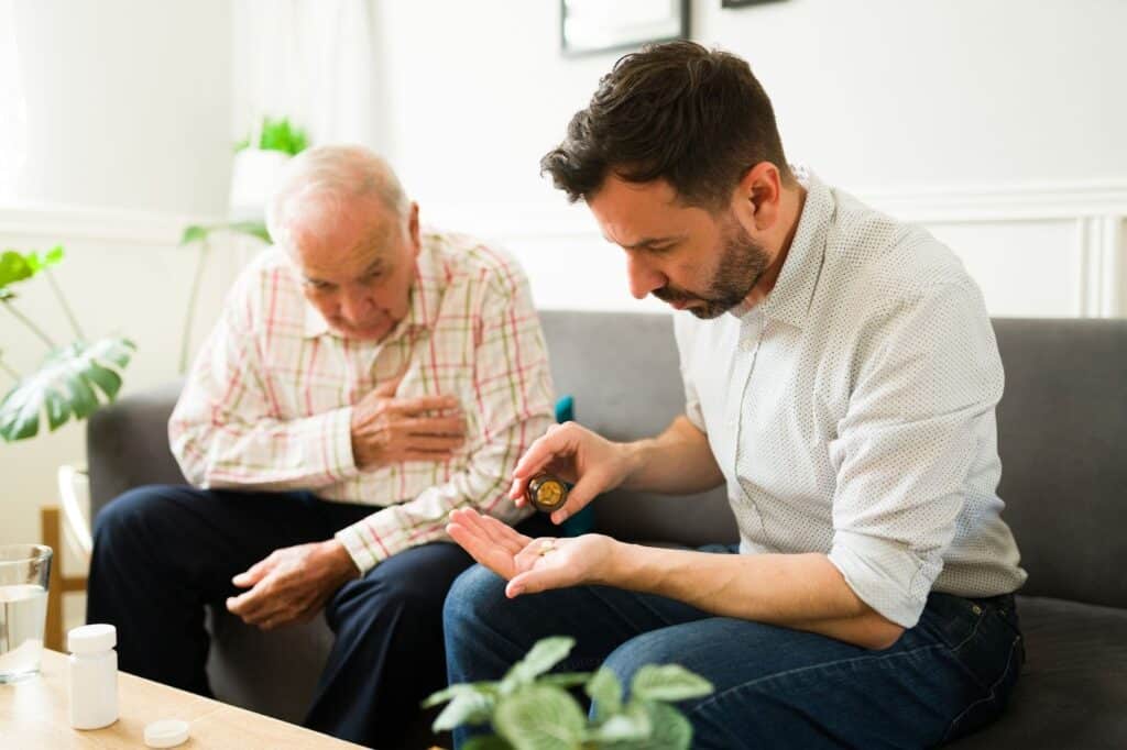 Adult son helping older parent with daily medication at their home.