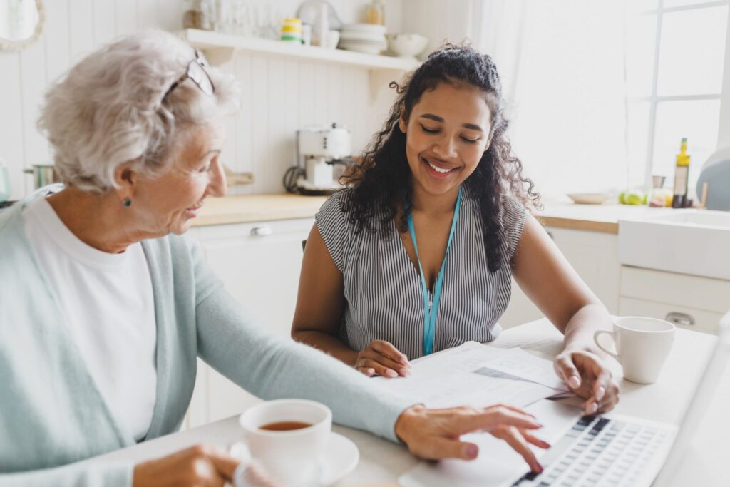 A family caregiver and an older adult sitting together at a kitchen table.