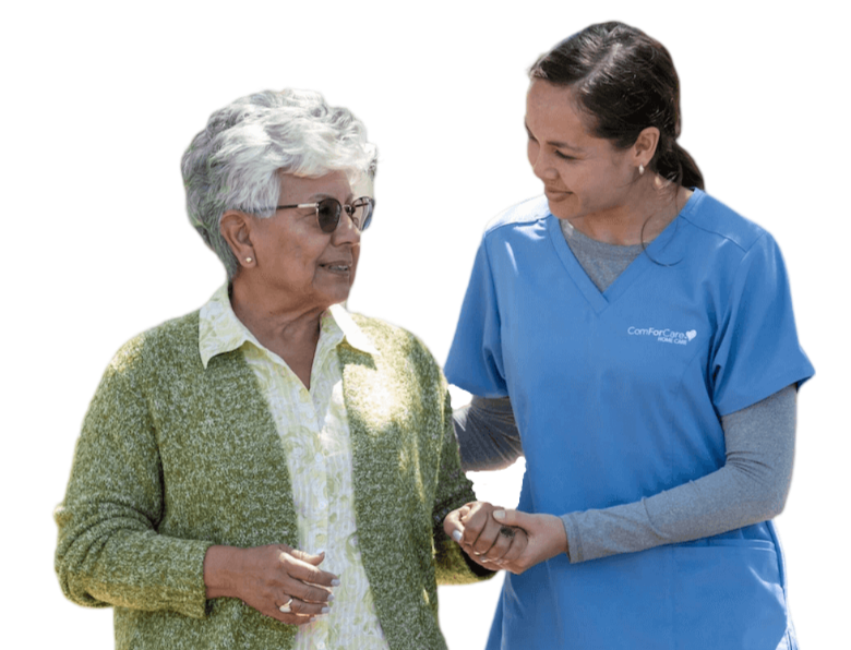 ComForCare Caregiver walking closely with a senior woman outside on a sunny day.