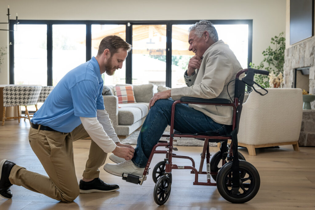 ComForCare Caregiver assisting a male client with his shoes while he is in wheelchair. 