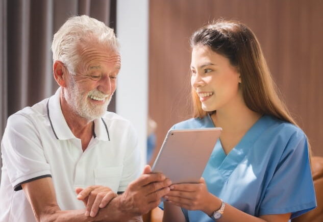 ComForCare Cargiver and a senior male client looking at an iPad/tablet electronic device together, without worrying about online scams.