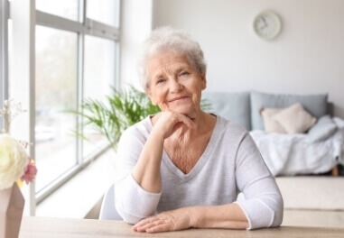 A senior woman sitting across table smiling at the camera.
