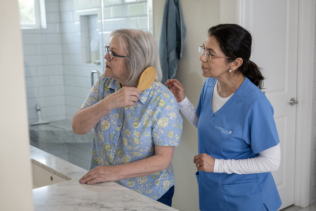ComForCare Caregiver standing by while senior woman client is brushing her hair