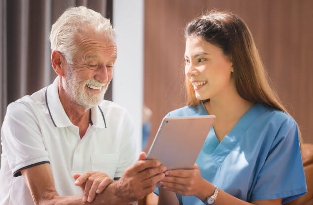 ComForCare Caregiver and a senior male client looking at an ipad/tablet electronic device, joyfully without worry about scams.