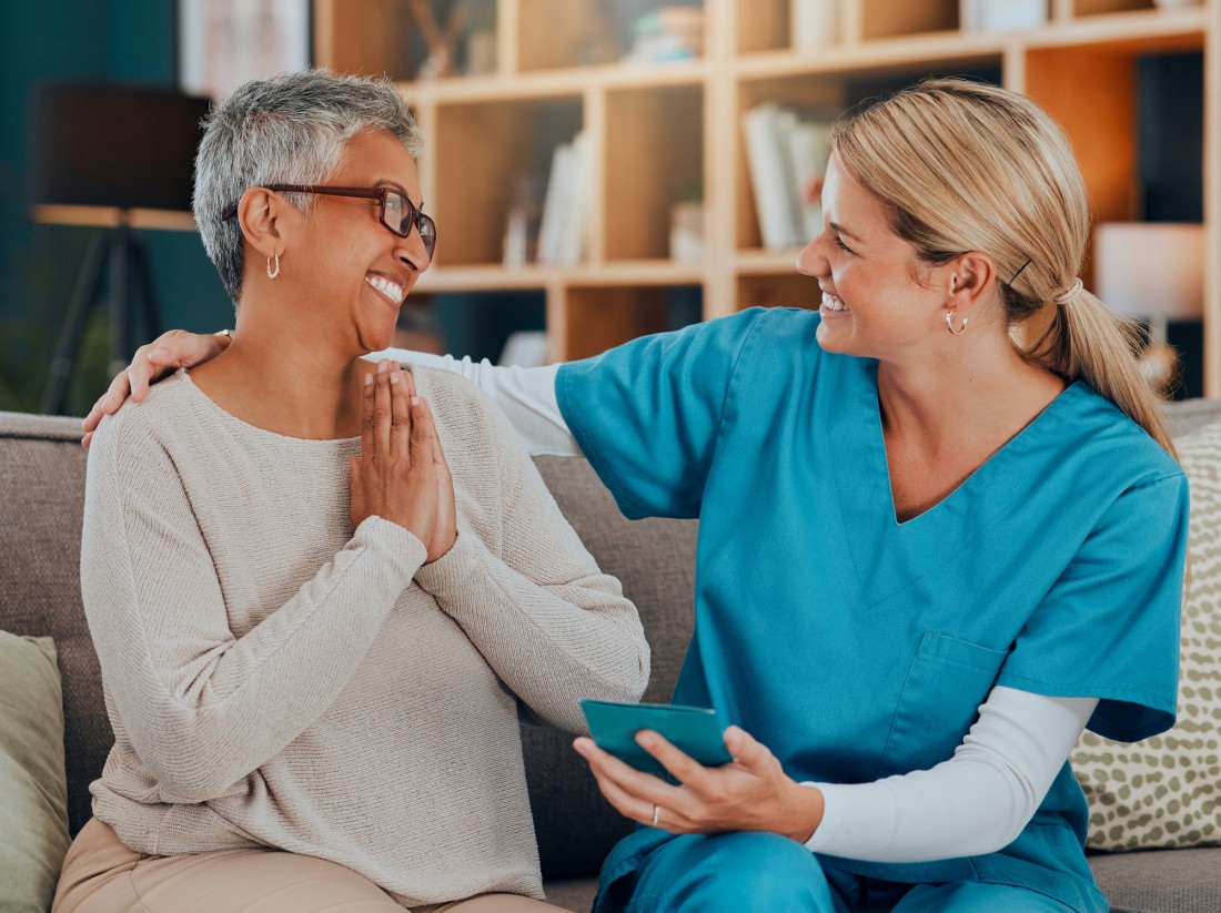 A caregiver puts her arm around an older lady while smiling as they look at medical results