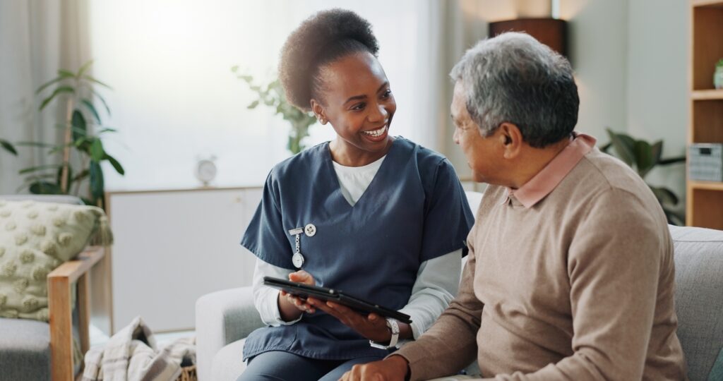 A caregiver happily showing a tablet to an older gentleman.