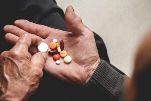 An older person looking over a handful of pills in their hand.