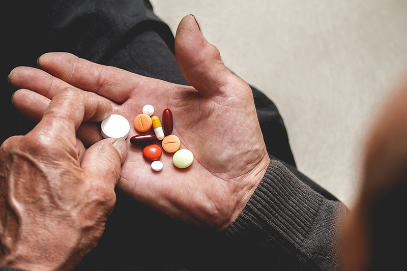An older person looking over a handful of pills in their hand.